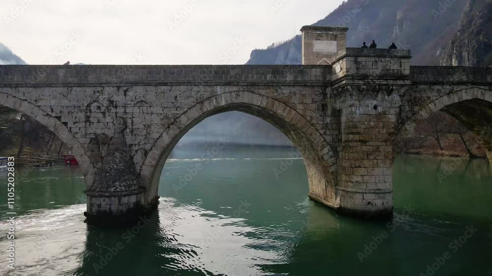 Exploring the scenic beauty of an ancient stone bridge over a calm river in a mountainous region during winter Exploring the scenic beauty of an ancient stone bridge over a calm river in a mountainous region during winter