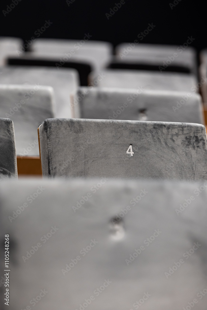 Rows of empty seats in a cinema hall, front side of the seats with numbers. Close-up with shallow depth of field