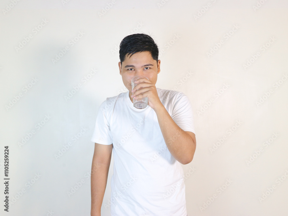 happy young asian man drinking water from glass over white background happy young asian man drinking water from glass over white background