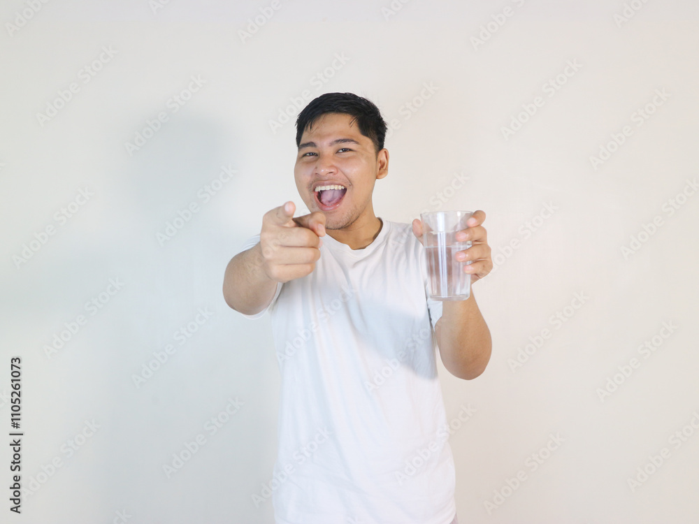 excited Asian man holding a glass of water and pointing forward excited Asian man holding a glass of water and pointing forward