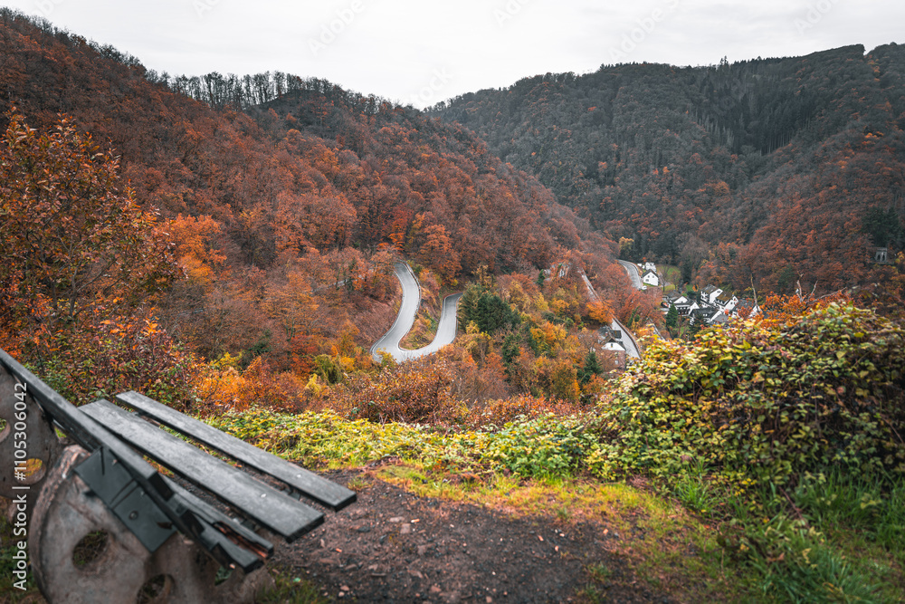 Fototapeta premium Bank vor herbstlicher Berglandschaft mit geschwungener Straße