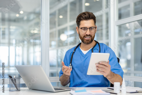 Doctor smiling using tablet at desk with laptop in modern office. Medical professional embracing technology for communication and patient care.