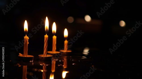 Image: 4 candles with bright flames on reflective glass, arranged symmetrically. Dark background enhances warm glow, evoking tranquil ambiance. photo