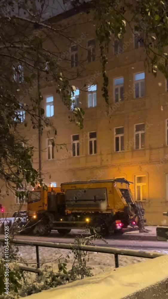 Snow-removal truck clears streets in winter storm at night in urban area Snow-removal truck clears streets in winter storm at night in urban area