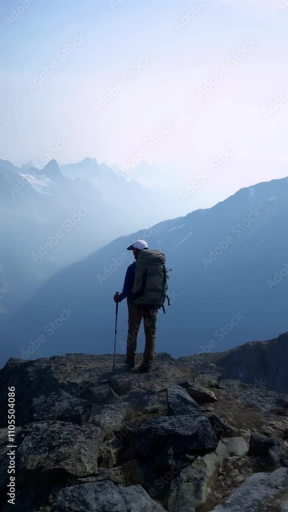 Hiker standing on mountain peak with backpack, vertical footage Hiker standing on mountain peak with backpack, vertical footage