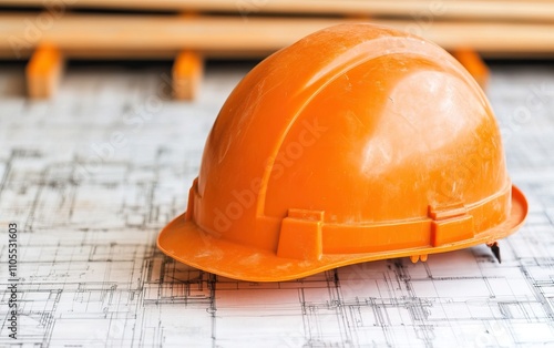 An orange hard hat rests on architectural blueprints, symbolizing construction safety and planning. photo