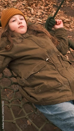 Young girl lying on a swing in an autumn park at a playground