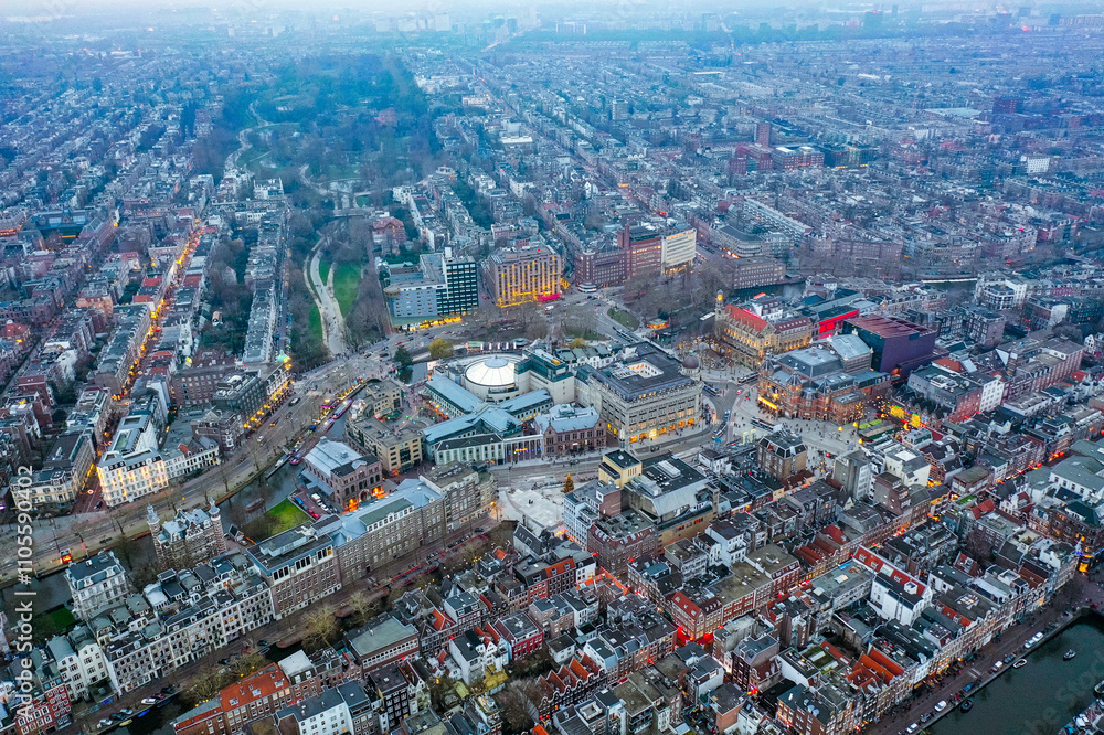 Obraz premium Vibrant aerial view of Amsterdam's Leidseplein district illuminated at dusk, showcasing iconic Dutch architecture, bustling nightlife, and serene green spaces