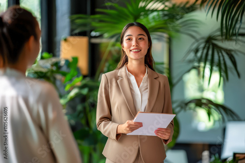 Businesswoman in a beige suit holding documents, confidently speaking during a meeting in a bright office with greenery. photo