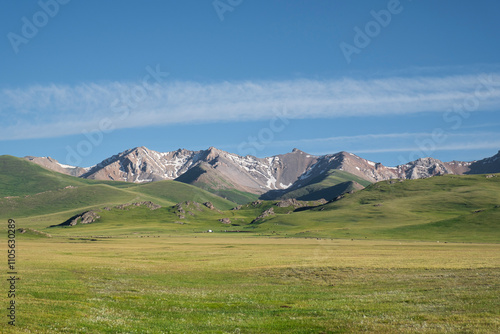 Vast green meadows meet majestic mountains at Song-Kol Lake under a clear blue sky, Kyrgyzstan, Central Asia