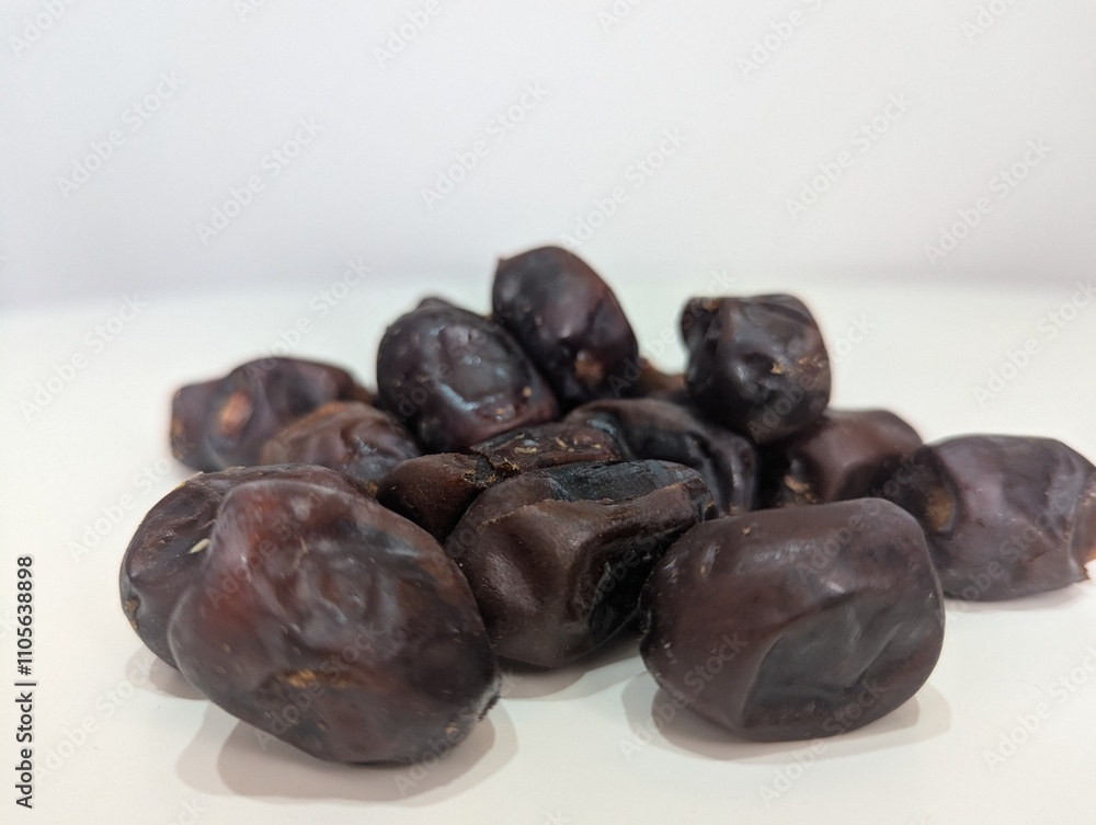 Close-up of a pile of dates on a white table, highlighting their glossy texture and rich caramel color. This composition underscores their role as a natural energy booster Close-up of a pile of dates on a white table, highlighting their glossy texture and rich caramel color. This composition underscores their role as a natural energy booster