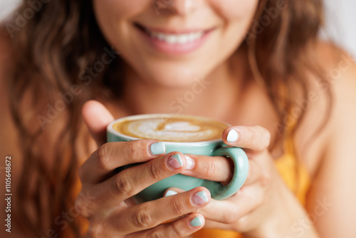 Close up of a young woman's hands holding a cup of specialty coffee with a drawing of a heart. Concept of tranquility and calm, tasting a good coffee.