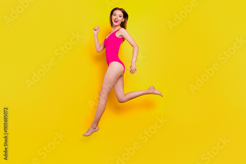 Run to meet the summer. Full-legs portrait of fit sporty girl inred swimsuit jumping over in the air looking at camera isolated on yellow background photo