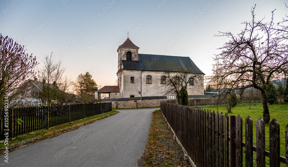 A serene view of the Church of the Nativity of the Virgin Mary in the village of Mlynicky Dvur, showcasing its architectural beauty and peaceful rural surroundings