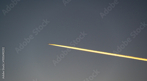 Obraz na płótnie A stunning sunset view of a flying airplane, captured from the ground, with fiery condensation trails glowing in the warm light of the setting sun w salonie