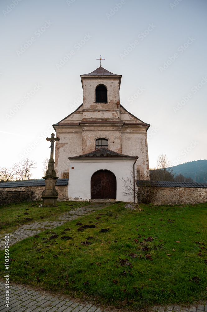 A serene view of the Church of the Nativity of the Virgin Mary in the village of Mlynicky Dvur, showcasing its architectural beauty and peaceful rural surroundings