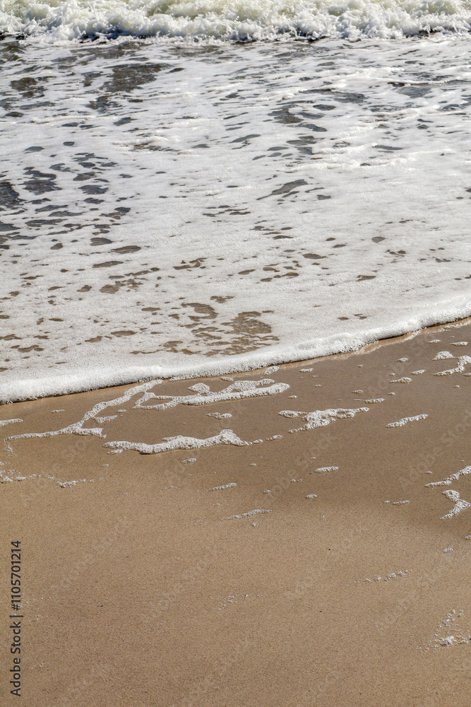 Detailed view of foamy ocean water gently meeting the smooth sand on a sunny beach day. Detailed view of foamy ocean water gently meeting the smooth sand on a sunny beach day.