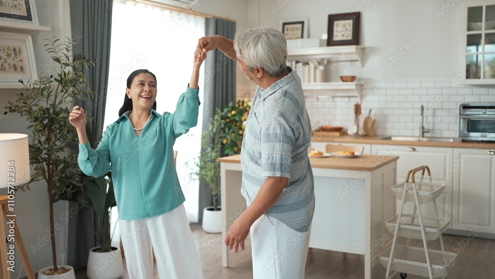 Fototapeta premium Happy grandfather and grandmother with casual cloth holding hand and dancing together at home. Lovely senior couple moving to music and spending time together while supporting at kitchen. Myrmidon.