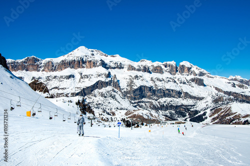Obraz na płótnie Easy ski slope with skiers and chairlift ski lift in Arabba ski resort in Dolomites, Italy. Sella Group mountain massif in the background. Blues sky with copy space w salonie