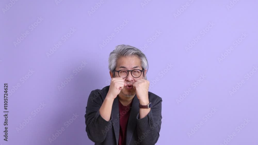 A senior East Asian businessman in a blazer stands against a purple background. A senior East Asian businessman in a blazer stands against a purple background.