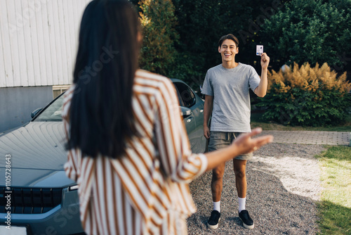 Happy young man showing drivers license to mother standing in back yard