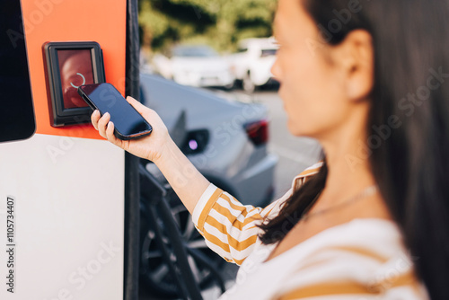 Over the shoulder view of mature woman doing mobile payment at electric vehicle charging station photo