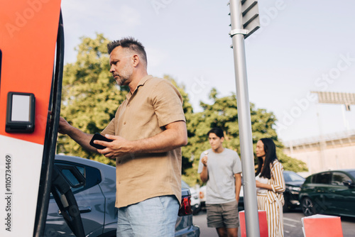 Low angle view of mature man doing mobile payment at electric vehicle charging station photo