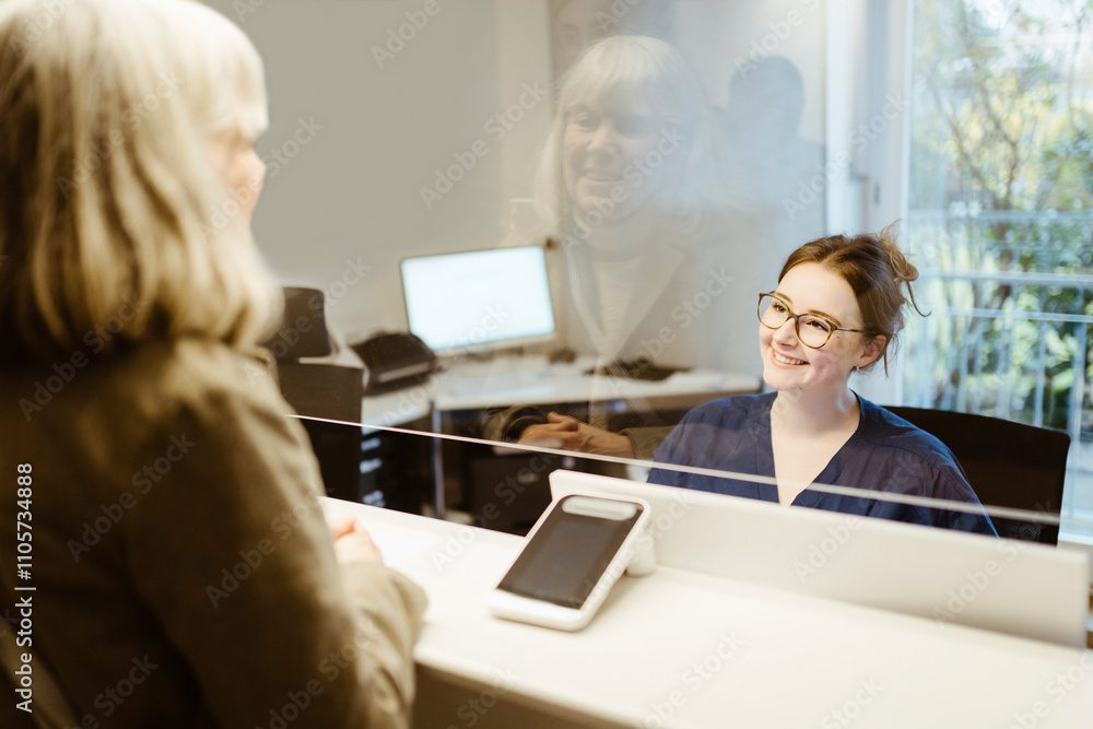 Smiling female medical worker assisting senior patient at reception desk in hospital Smiling female medical worker assisting senior patient at reception desk in hospital
