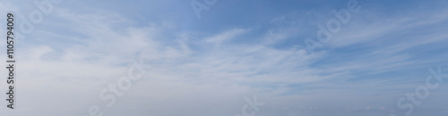 Wide-angle landscape photograph capturing a calm blue sky with soft white cirrus clouds, evoking tranquility and serenity.