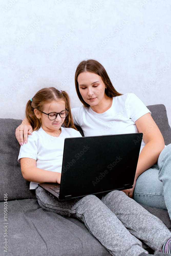 A mother working from home with her daughter, both shopping online using a laptop. The woman hugs her child, creating a cozy and productive home office atmosphere in the living room.