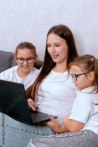 A young mother or nanny with children in the living room, using a laptop. A warm, family-focused scene, perfect for themes of remote work, online learning, or childcare at home. photo