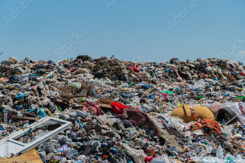 A large pile of garbage dominates the landscape, showcasing discarded plastic, food waste, and other debris. The site indicates severe pollution and lack of effective recycling systems