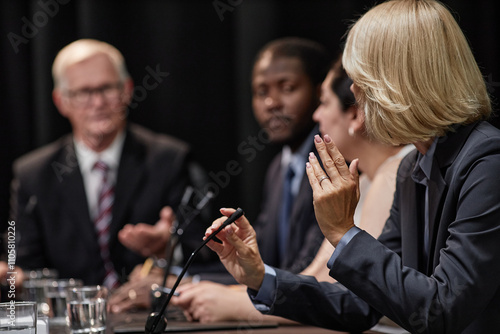 Rear view of female official speaking into microphone asking politician question during political debate or press conference meeting room, copy space