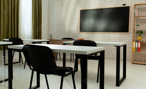 Empty modern school classroom with desks, chairs and chalkboard at daylight, workspace for learning and teaching. Seat angle view.