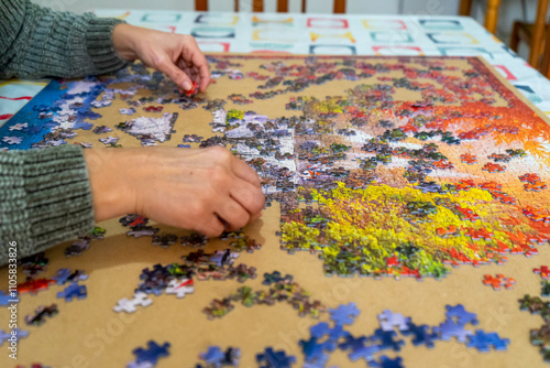 Horizontal close-up image of a woman's hands searching for the right piece to solve the puzzle, entertainment concept.