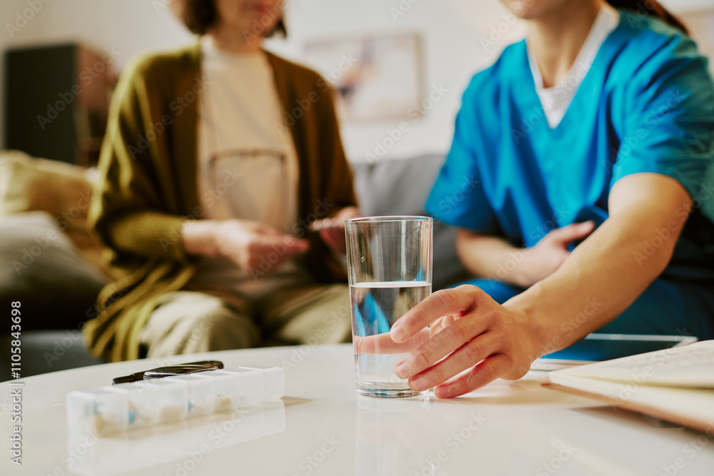 Healthcare professional assisting senior woman at home by providing medication support, person in blue scrubs ensuring proper care for elderly individual sitting in living room Healthcare professional assisting senior woman at home by providing medication support, person in blue scrubs ensuring proper care for elderly individual sitting in living room