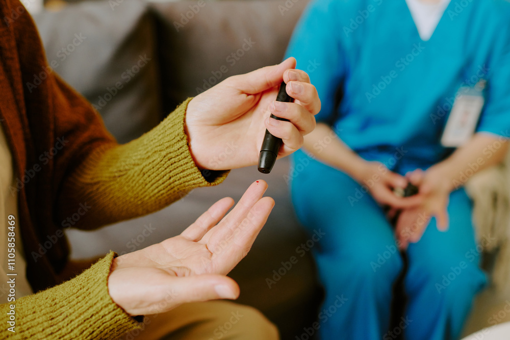 Obraz premium Elderly person checking blood sugar levels with glucometer while sitting on couch, assisted by healthcare professional wearing blue scrubs and holding medical report