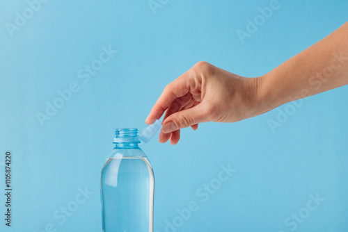 Slika na platnu Hand demonstrating the new stationary tethered caps on PET plastic water bottles on the blue background, designed to reduce plastic waste