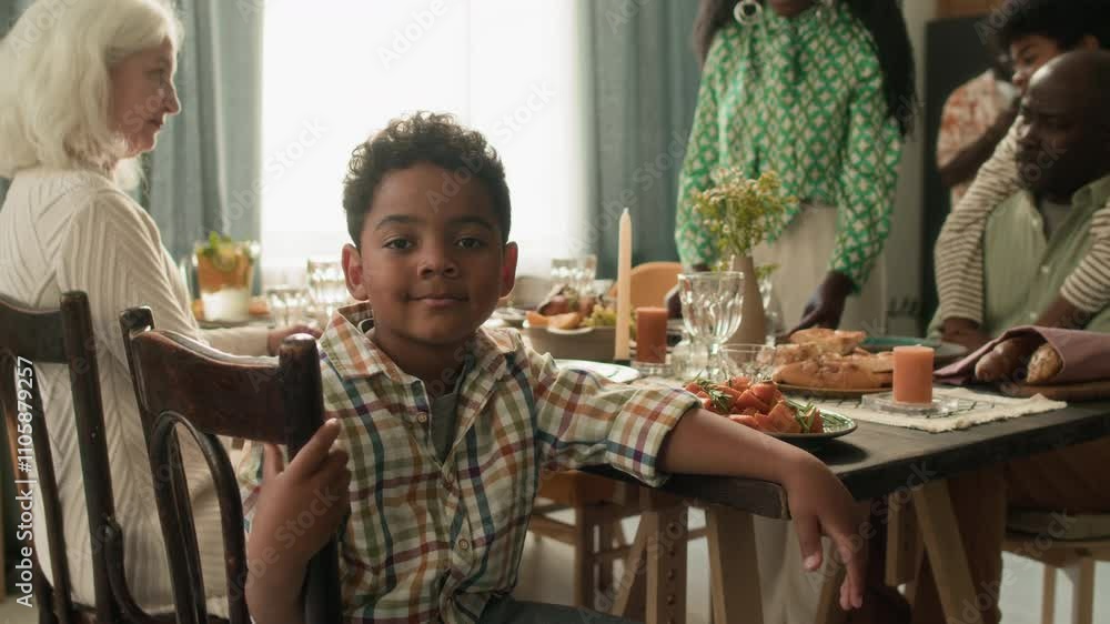 Portrait of African American preschool boy posing for camera while sitting at festive table with family Portrait of African American preschool boy posing for camera while sitting at festive table with family
