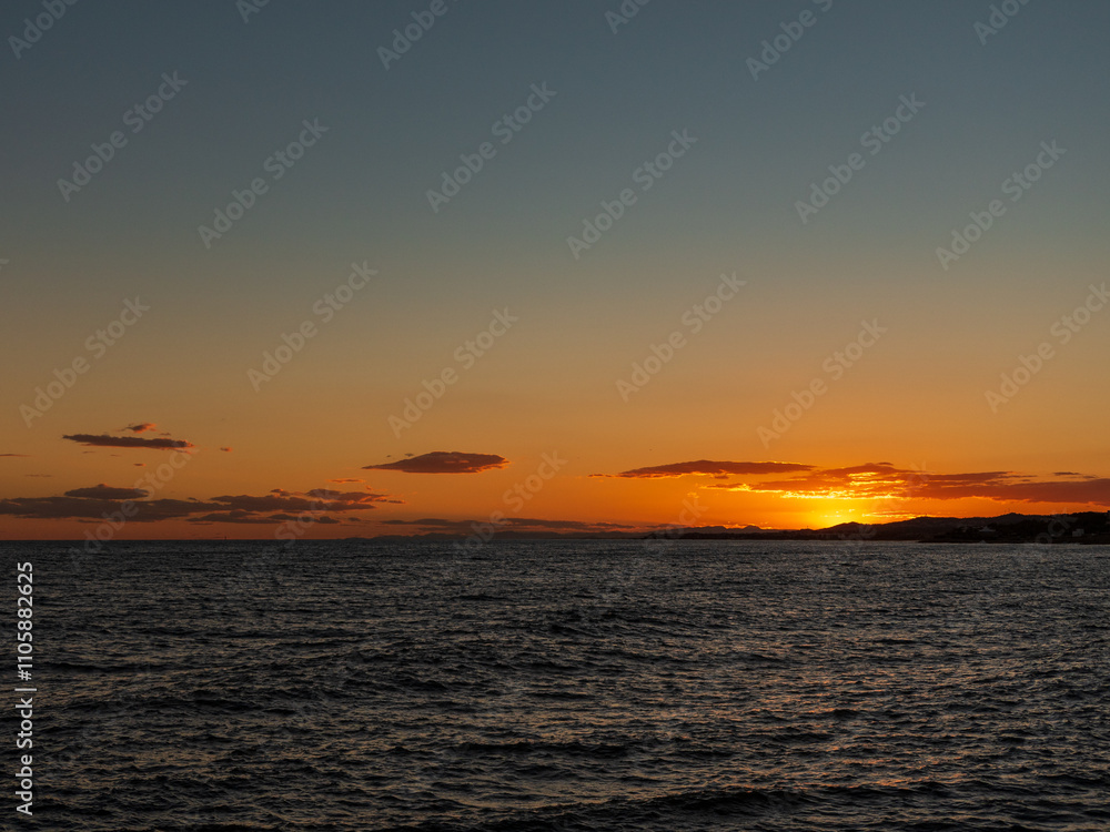 Atardecer en el mar con cielo despejado y nubes anaranjadas, reflejando tonos cálidos sobre el agua ondulante. Perfecta escena de naturaleza serena y vibrante.