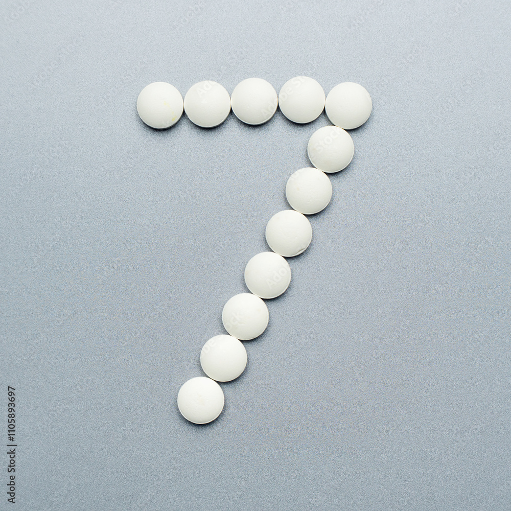 The number 7 made of white pills on a grey background The number 7 made of white pills on a grey background