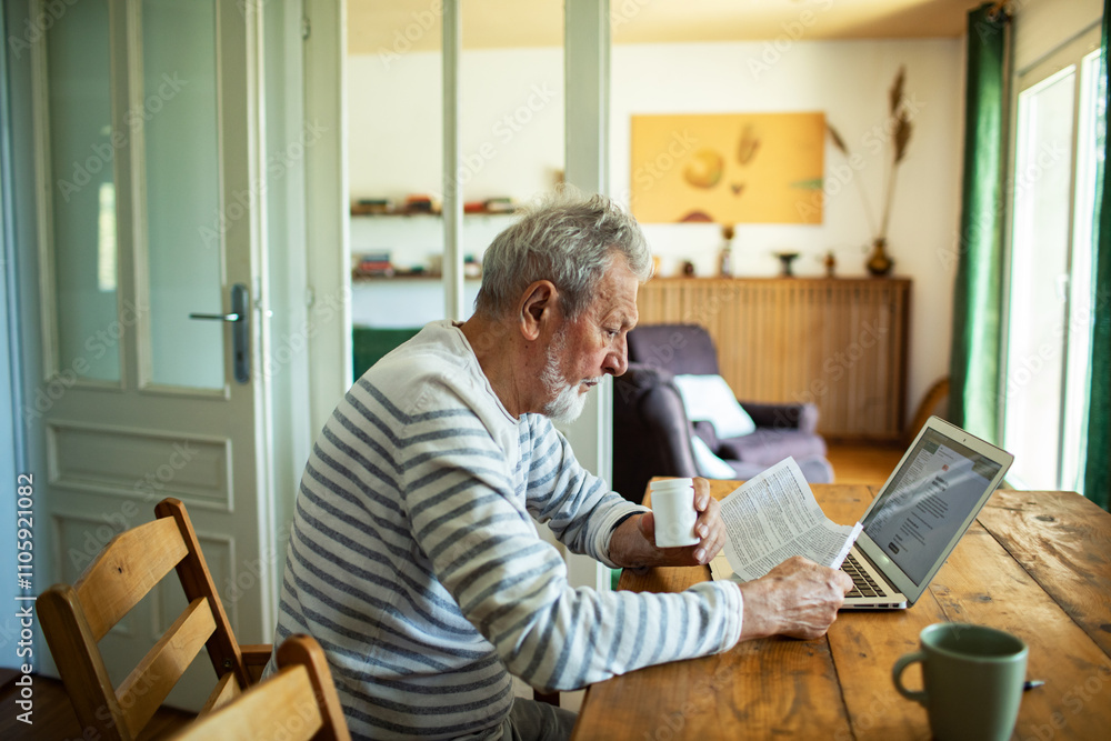 Stressed senior man reading bills on kitchen table with laptop Stressed senior man reading bills on kitchen table with laptop