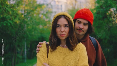 A woman appears sad in the park, her boyfriend approaching to console her with a hug. Despite his care, she walks away, leaving him standing alone. the guy shows her the middle finger in response