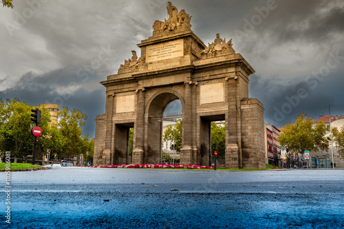 A large archway with a red sign in front of it. The archway is surrounded by trees and a few cars are parked in the area photo