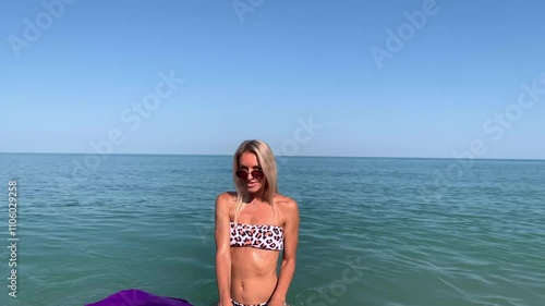 Beautiful slim sexy blonde woman in sunglasses floats on an inflatable mattress in the sea. Enjoys, sunbathes, smiles.