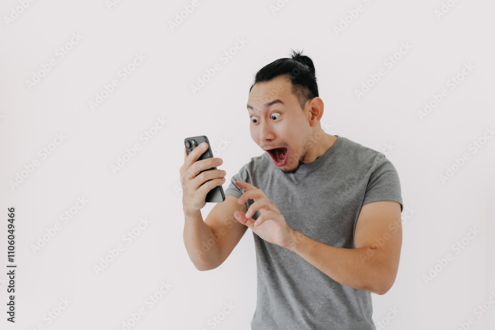 Shock and wow face Asian man in grey t-shirt use smartphone app on white. Shock and wow face Asian man in grey t-shirt use smartphone app on white.