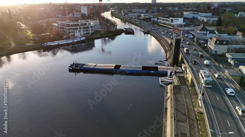 Barge navigating calm waters near urban surroundings at sunset