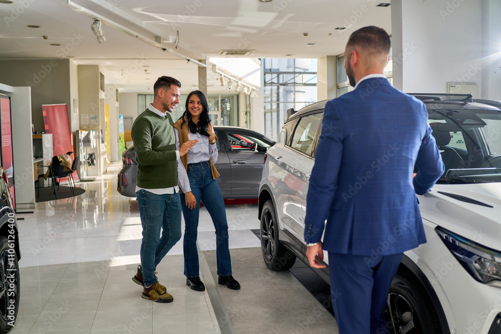Car dealership scene featuring a salesman showing a couple a car, he is gesturing towards the car, while the couple appears engaged and interested. Car dealership scene featuring a salesman showing a couple a car, he is gesturing towards the car, while the couple appears engaged and interested.