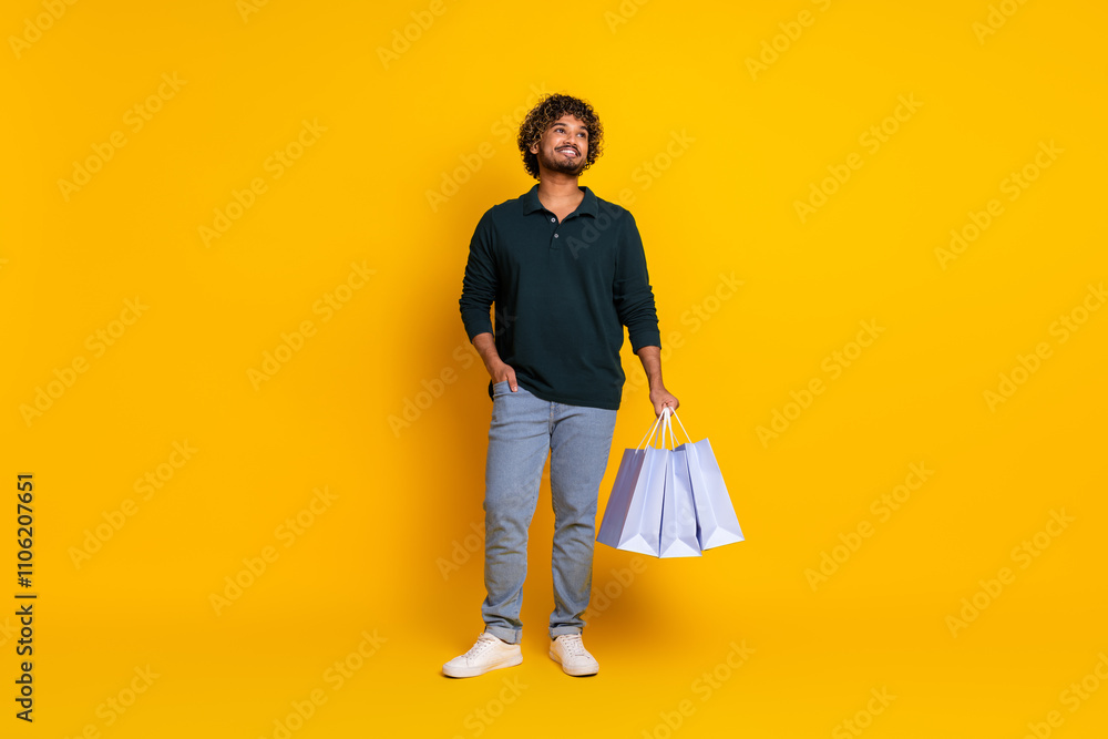 Young man in black shirt holding shopping bags against yellow background, looking joyful perfect for advertising promotional content Young man in black shirt holding shopping bags against yellow background, looking joyful perfect for advertising promotional content