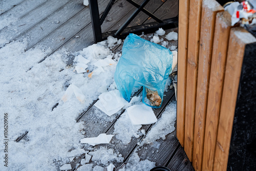 A blue plastic bag is laying casually on a wooden deck that is presently covered in a thick layer of snow, creating a striking contrast between the colors and materials of the scene photo